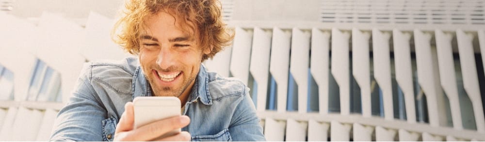 Homme frisé qui rit devant son smartphone