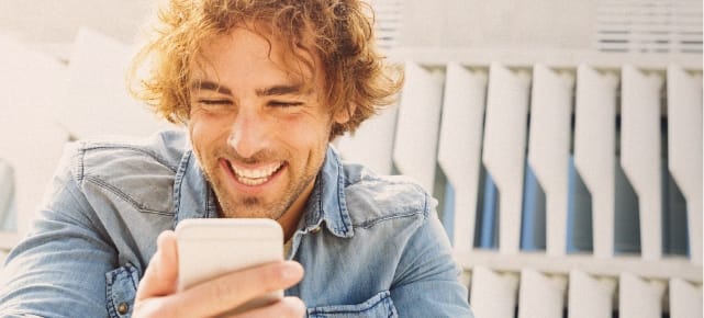 Homme frisé qui rit devant son smartphone